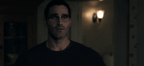 a man wearing glasses and a black shirt is standing in a dark room