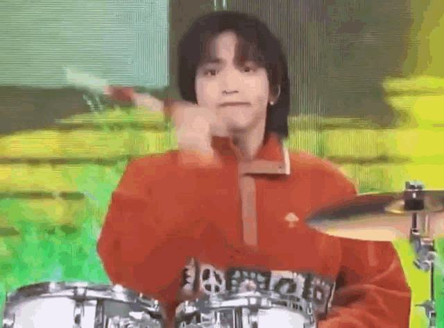 a man in a red sweater is playing drums on a stage .