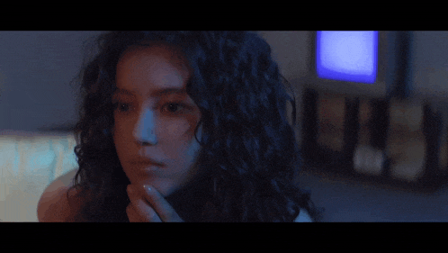 a woman with curly hair is looking at the camera in front of a blue television .