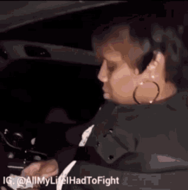 a woman is sitting in the driver 's seat of a car and looking at her phone .