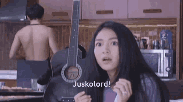 a woman is holding a guitar in front of a man without a shirt .