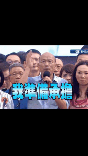 a man speaking into a microphone in front of a crowd with chinese writing on the screen