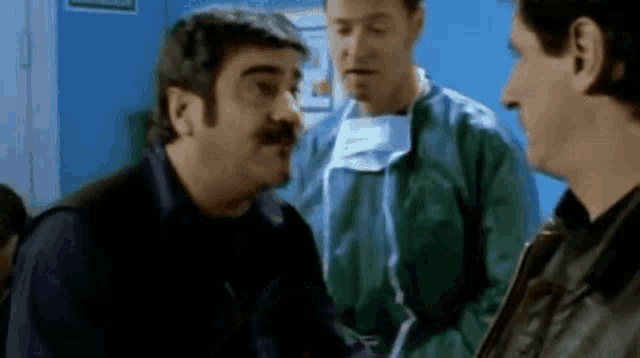 a group of men are standing next to each other in a room . one of the men is wearing a surgical mask .