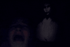 a man is screaming in the dark while a ghost is standing behind him .