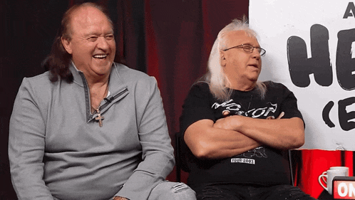 two men are sitting in front of a sign that says " a he "