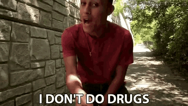 a man in a red shirt says i do n't do drugs in front of a brick wall