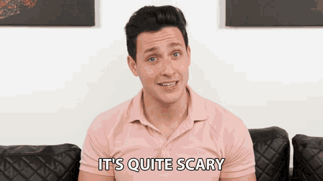 a man in a pink shirt says it 's quite scary in front of a black couch