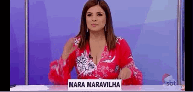 a woman in a red shirt is sitting at a table with a sign that says `` mara maravilha '' .