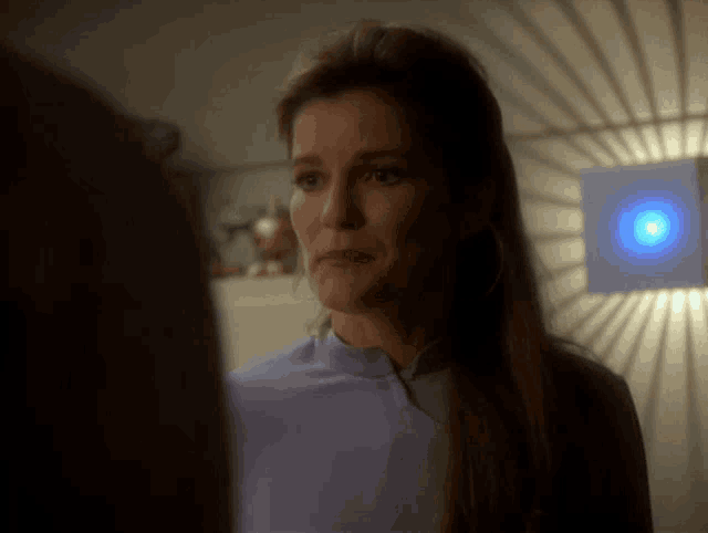a woman in a purple shirt looks at a man in a dark room