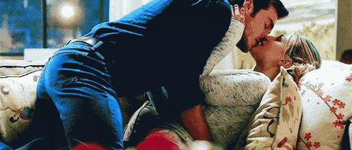 a man and woman are kissing on a couch .