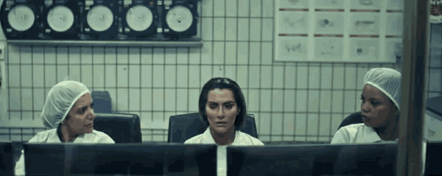 a group of women in lab coats are sitting in front of a computer screen