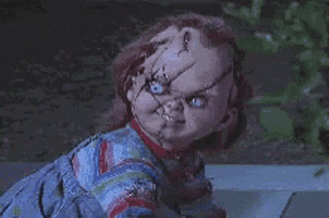 a chucky doll is standing on a sidewalk in the dark .