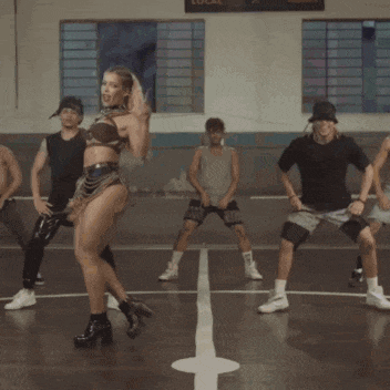 a woman in a crop top and shorts is dancing in front of a group of men