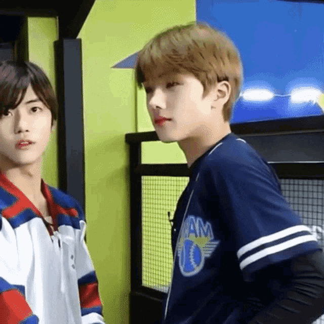 two young men are standing next to each other in a room and one of them is wearing a baseball jersey .