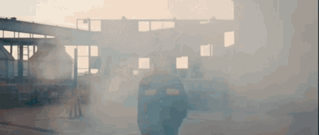a man in a black jacket is standing in front of a building covered in smoke .