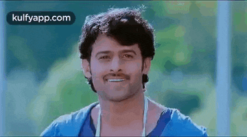 a man in a blue shirt is smiling while standing in front of a green background .