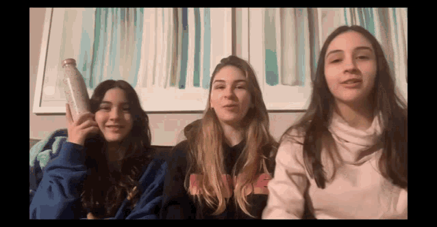three young women are sitting next to each other and one of them is holding a water bottle