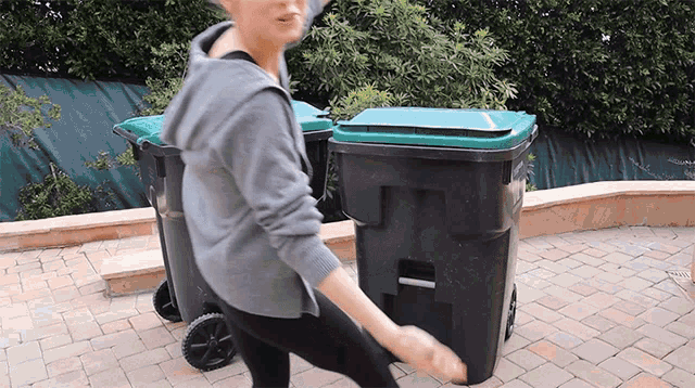 a woman is pushing two trash cans on a brick sidewalk