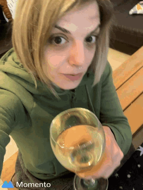 a woman in a green hoodie is holding a glass of wine in front of a momento icon