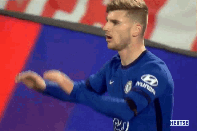 a soccer player wearing a blue shirt with hyundai written on the sleeve is standing on a field .