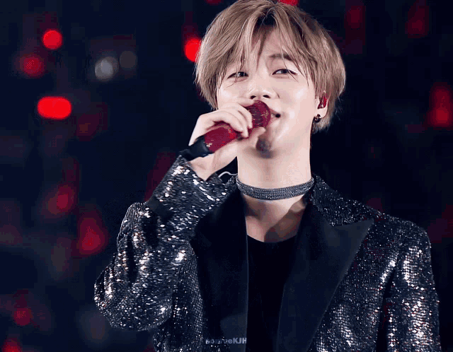 a man in a sequined jacket is singing into a microphone with a choker around his neck