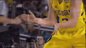 a basketball player wearing a michigan jersey is giving a high five