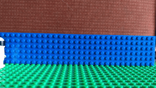 a lego figure wearing a helmet is walking across a green and blue lego surface