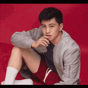 a young man in a grey jacket and red shorts is sitting on a red surface .