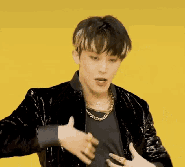 a young man wearing a black jacket and a gold necklace is taking off his shirt .