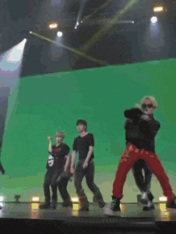 a group of people are dancing on a stage in front of a green background
