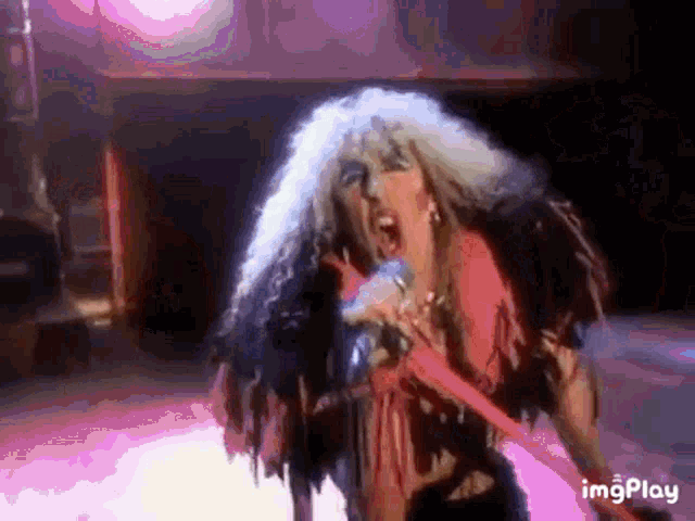 a woman singing into a microphone with a purple background and the word imgplay at the bottom