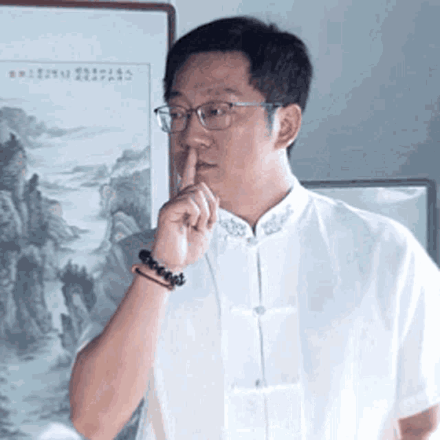 a man wearing glasses and a bracelet is covering his mouth with his finger