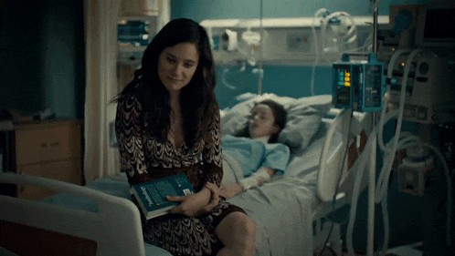 a woman sits next to a child in a hospital bed holding a book that says emergency medicine