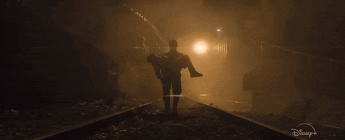 a man is carrying another man in his arms in a dark tunnel with a disney logo in the corner