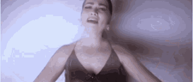 a woman in a black tank top is singing into a microphone while standing in front of a white wall .