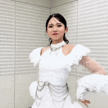 a woman in a white dress stands in front of a wall
