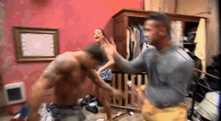 a group of men are fighting in a room with a woman in the background .