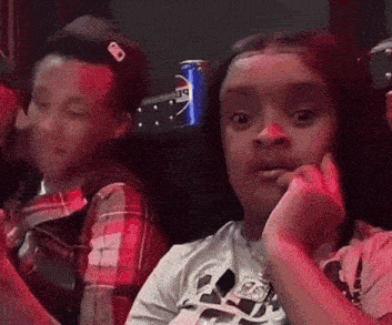 a boy and a girl are sitting next to each other in a dark room with a pepsi can in the background .