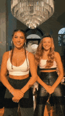 two young women are standing next to each other in front of a chandelier .