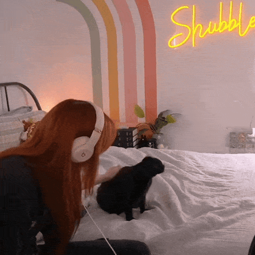 a woman wearing headphones is sitting on a bed with a neon sign that says shubble