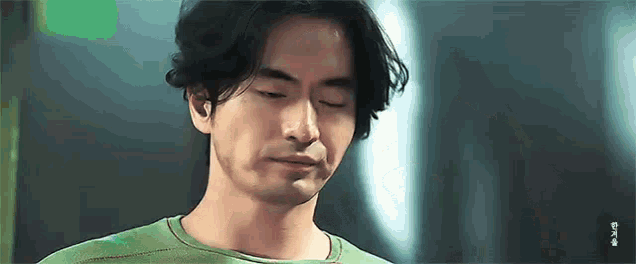 a man with long hair and a beard is wearing a green shirt and looking down with his eyes closed .