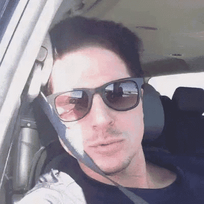 a man wearing sunglasses is sitting in a car with his seat belt on