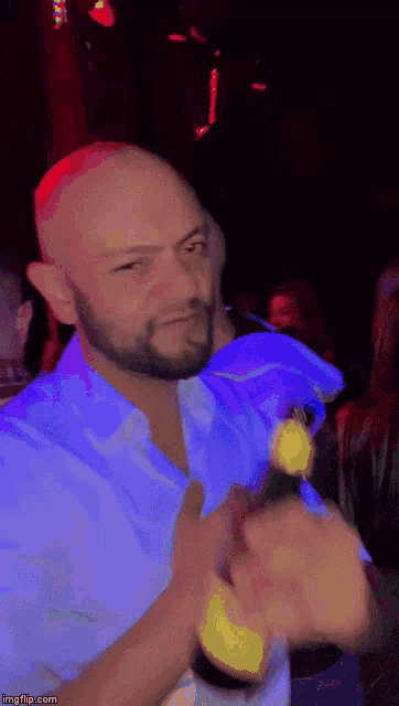 a man with a beard is holding a bottle of beer in a dark room