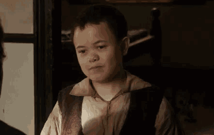 a young boy wearing a vest and a shirt is standing next to a man in a room .