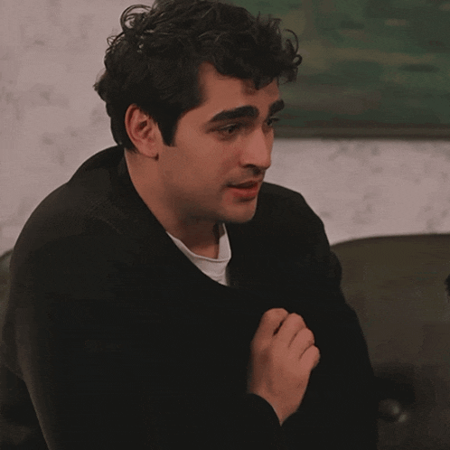 a man in a black sweater sits on a couch looking down