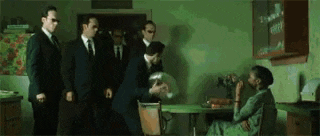 a group of men in suits and sunglasses are standing around a woman in a green room .