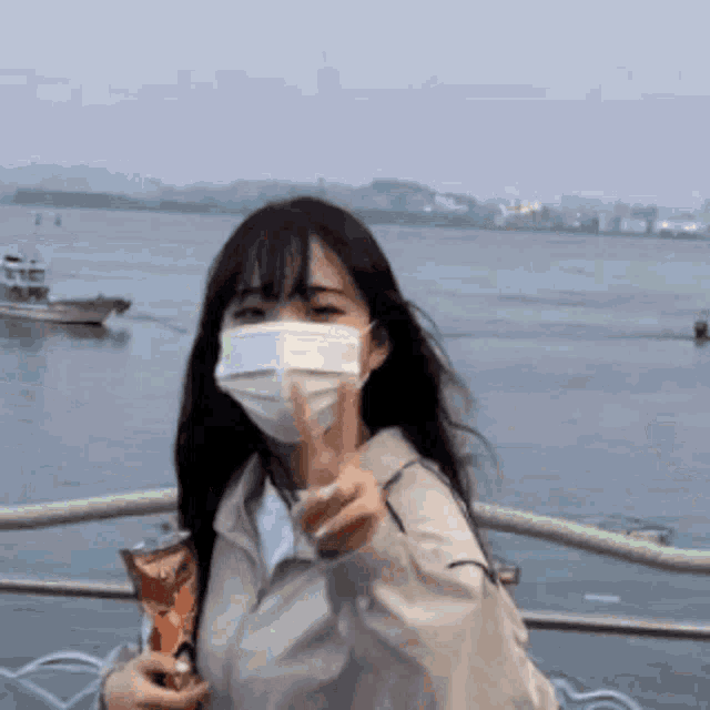 a woman wearing a mask is holding a bag of chips and giving a peace sign .