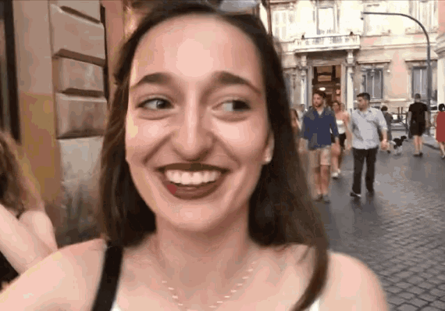 a woman is smiling and looking at the camera while walking down a street
