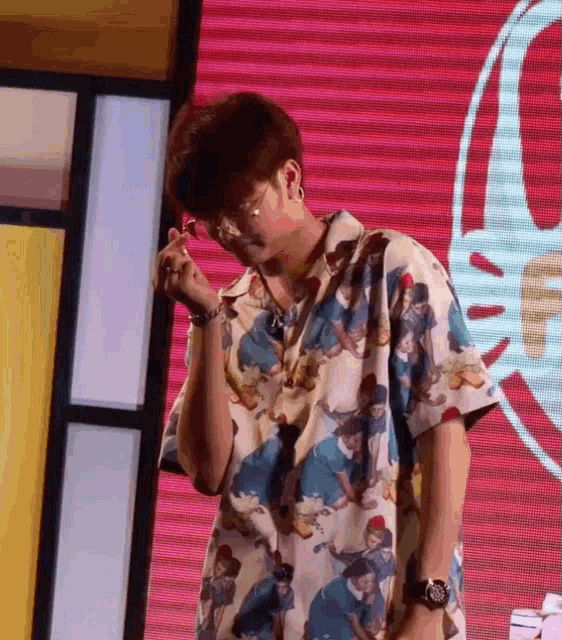 a man wearing a hawaiian shirt and glasses stands in front of a large screen