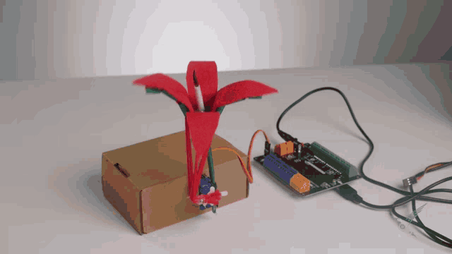 a flower made out of a cardboard box next to a microcontroller board